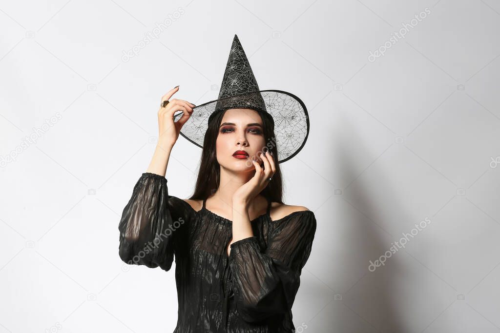 Beautiful woman dressed as witch for Halloween party on light background