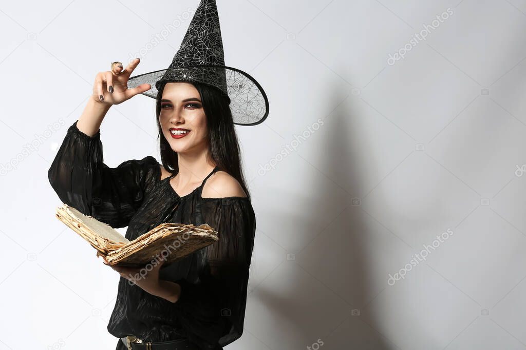 Young witch with spell book on light background