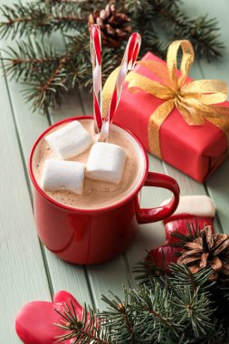 Bir fincan sıcak kakao, köknar dalları ve renkli ahşap arka planda hediye kutusu.