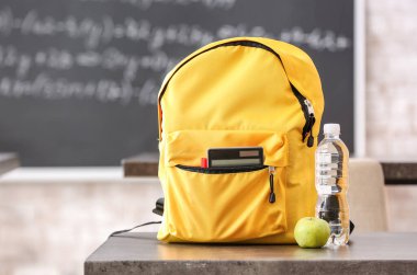 Okul çantası, su ve elma şişesi sınıfın masasında.