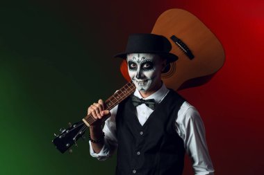 Yüzünde boyalı kafatası ve gitarı olan genç bir adam. Meksika Ölüler Günü 'nün Kutlaması (El Dia de Muertos)