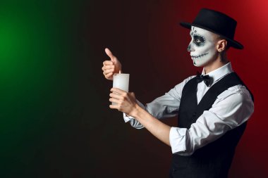 Yüzünde boyalı kafatası ve koyu arka planda mumu olan genç bir adam. Meksika Ölüler Günü 'nün Kutlaması (El Dia de Muertos)