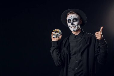 Meksika Ölüler Günü (El Dia de Muertos) için koyu arkaplanda boyalı yüzü ve şeker kafatası olan genç bir adam.