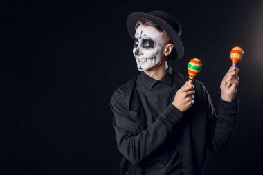 Yüzünde boyalı kafatası ve koyu arka planda marakas olan genç bir adam. Meksika Ölüler Günü 'nün Kutlaması (El Dia de Muertos)