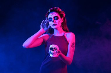 Meksika Ölüler Günü (El Dia de Muertos) için koyu arkaplanda boyalı yüzü ve şeker kafatası olan genç bir kadın.