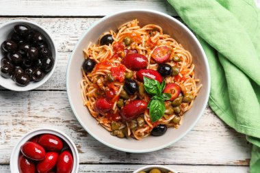 Bir kase lezzetli makarna Puttanesca ve beyaz ahşap arka planda malzemeler.