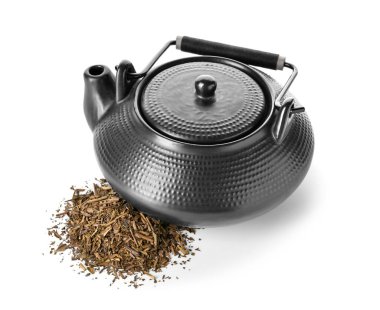 Çay demliği ve beyaz arka planda bir yığın kuru hojicha yeşil çayı.