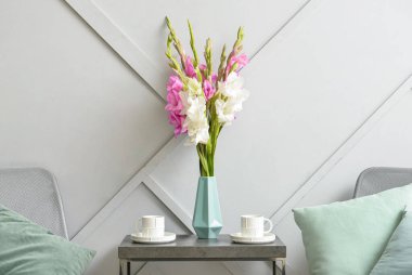 Glayolus çiçekli vazo ve masadaki kahve fincanları.