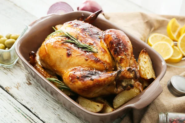 Baking dish with tasty chicken and potato on light wooden background, closeup