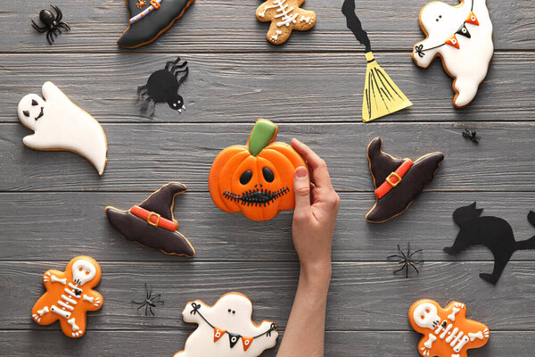 Female hand with tasty cookies for Halloween celebration on wooden background