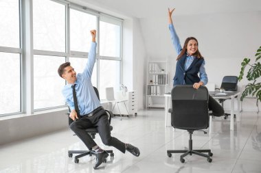 Mutlu meslektaşlar ofiste sandalye sürüyor.