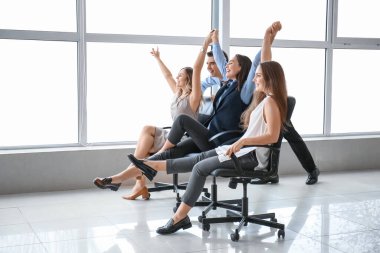 Mutlu meslektaşlar ofiste sandalye sürüyor.