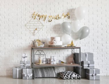 Doğum günü pastası ve tuğla duvarın yanında balonlar olan masa.