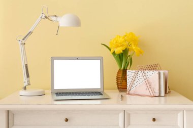 Modern dizüstü bilgisayarı ve ışık duvarına yakın çiçekleri olan şık bir iş yeri.