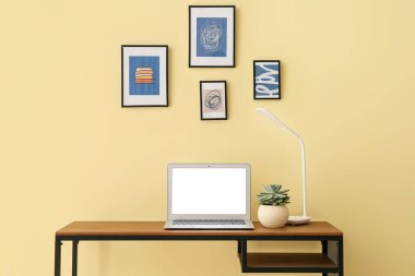 Modern dizüstü bilgisayarlı şık bir iş yeri ve renkli duvarların yanındaki resimler.