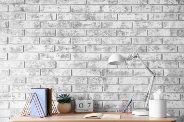 Not defterleri ve tuğla duvarın yanında modern lambası olan şık bir iş yeri.