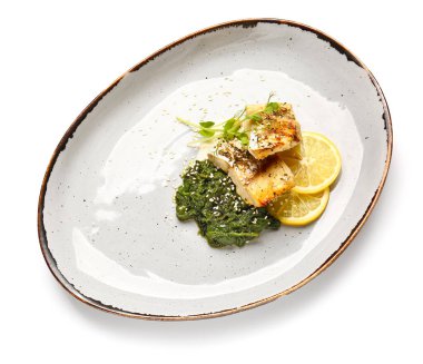 Lezzetli kızarmış morina filetosu, pesto sosu ve beyaz arka planda limon tabağı.