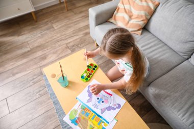 Masada suluboya resim yapan küçük bir kız.