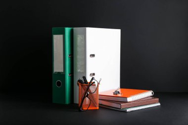 Koyu arkaplan üzerinde kırtasiye olan ofis dizinleri ve tutucu