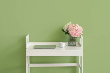 Ortanca çiçekli vazo ve laptop renkli duvarın yanındaki masada.