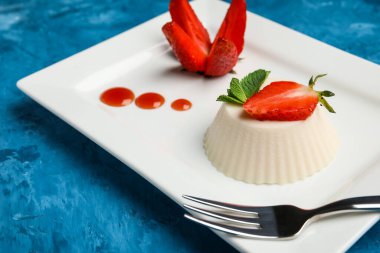 Mavi arka planda lezzetli çilekli panna cotta tabağı, yakın plan.