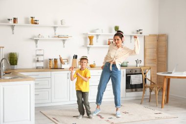 Genç kadın ve küçük oğlu mutfakta dans edip müzik dinliyorlar.