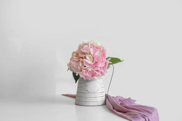 Vase with hydrangea flowers on table near light wall