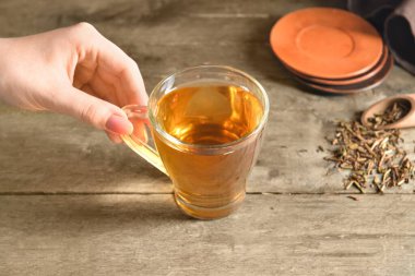 Ahşap arka planda bir fincan lezzetli hojicha yeşil çay tutan kadın, yakın plan.