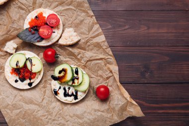 Çıtır pirinç krakerleri, kırmızı havyar ve ahşap arka planda sebzeli parşömen.