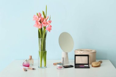 Odada gladyatör çiçekleri, ayna ve kozmetik ürünleri olan bir vazo.