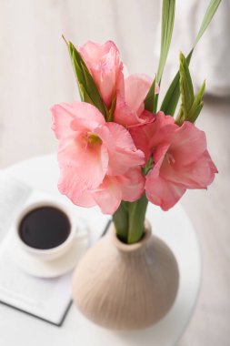 Gladiolus çiçekli vazo ve masada bir fincan kahve.