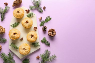 Mor arka planda lezzetli kıymalı turtalar, koniler ve köknar dallarıyla kompozisyon