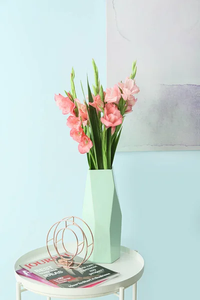 Vase with gladiolus flowers and magazines on table in room