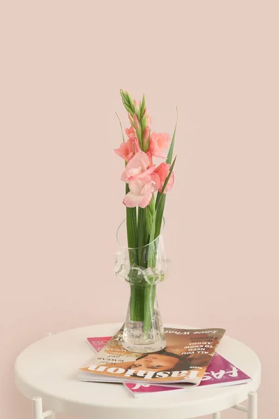 Vase with gladiolus flowers and magazines on table against color wall