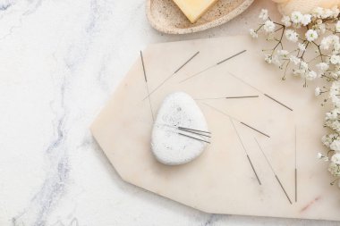 Beyaz zemin üzerinde akupunktur iğneleri ve spa taşı, üst görünüm