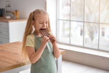 Sevimli küçük kız mutfakta çikolata yiyor.