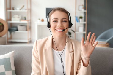 Kulaklıklı genç bir kadın evde video sohbeti yapıyor.