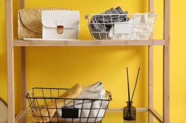 Sarı duvarın yanındaki rafta giysileri olan modern organizatörler.