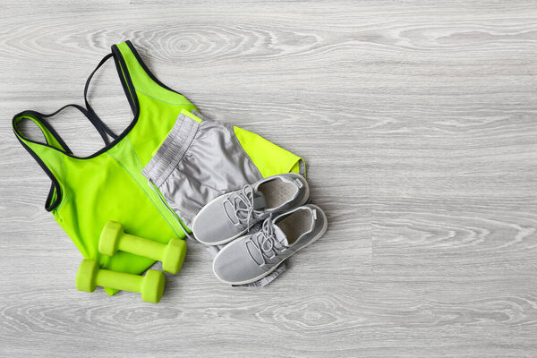 Sportswear, shoes and dumbbells on light wooden background