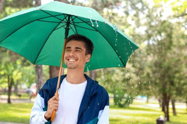 Parkta şemsiyesi olan yakışıklı genç adam.