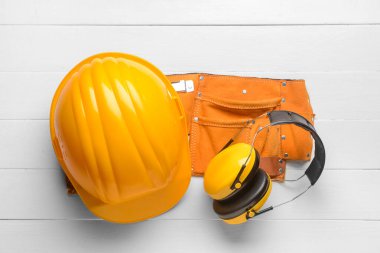 Kulak koruyucuları ve beyaz ahşap arka planda alet kemeri olan sert şapka