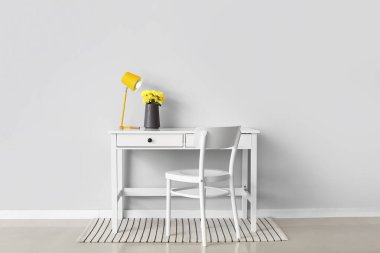 Vazoda çiçekler ve beyaz duvarın yanında modern lamba olan şık bir iş yeri.