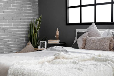 Büyük pencereli gri duvarın yanında rahat bir yatak ve çalar saat.