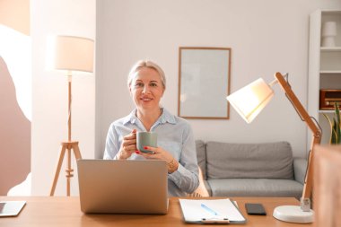 Ofiste kahve içen olgun bir kadın.