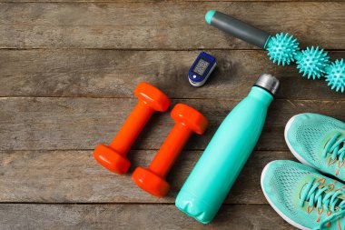 Nabız oksimetresi, su şişesi, ayakkabı ve spor malzemeleri ahşap arka planda.