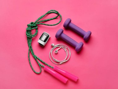 Nabız oksimetresi, dambıl, halat ve kulaklıklar renk arkaplanında