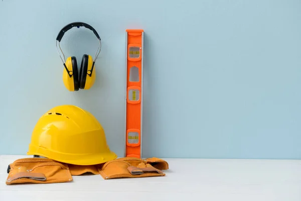 Hardhat with ear protectors and builder\'s supplies on color background