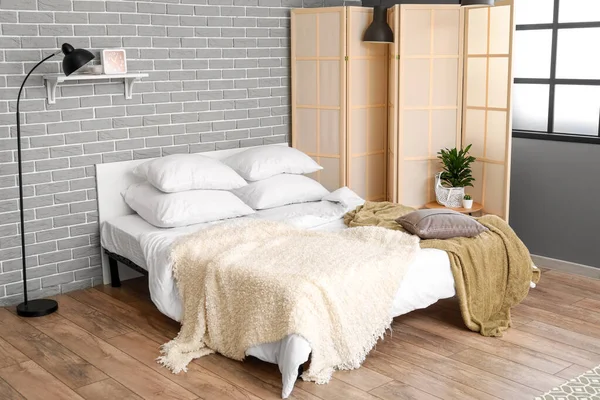 レンガの壁の近くの快適なベッド 床ランプと折りたたみ画面 — ストック写真