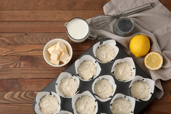 Baking tin with uncooked poppy seed muffins on wooden table