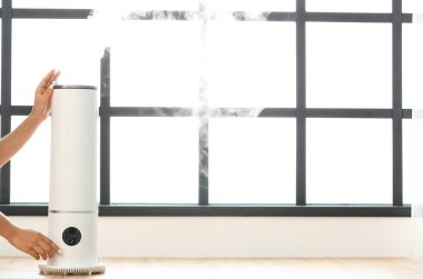 Kadın odasındaki modern nemlendiriciyi açıyor.